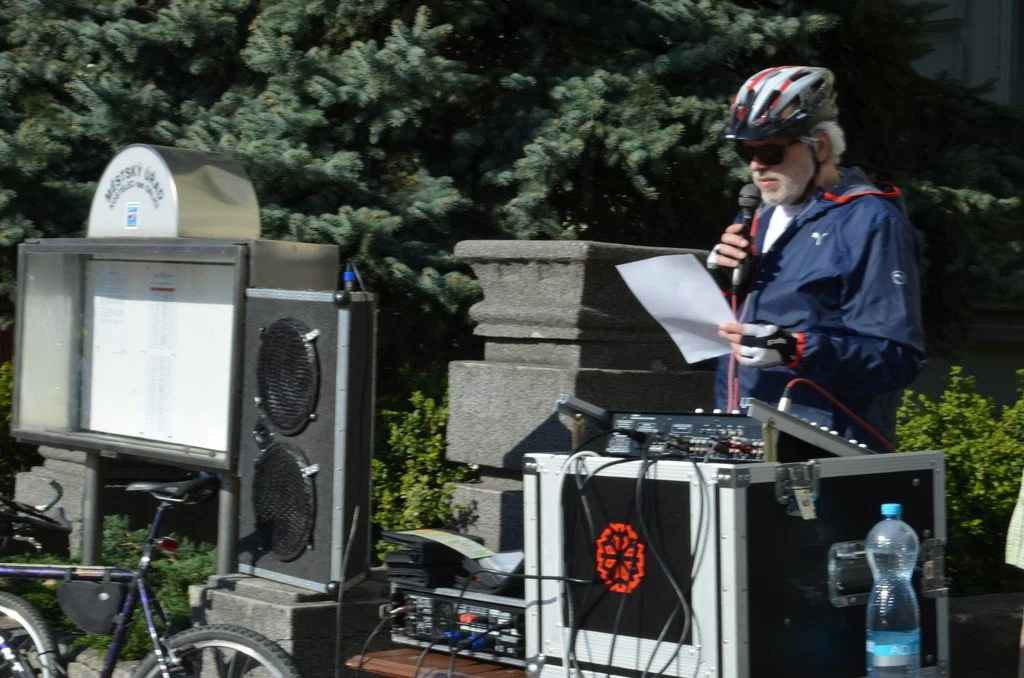 Muž s mikrofonem promlouvá k účastníkům cyklistické akce