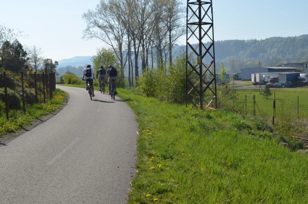 Cyklisté jedou po stezce kolem stožáru vysokého napětí