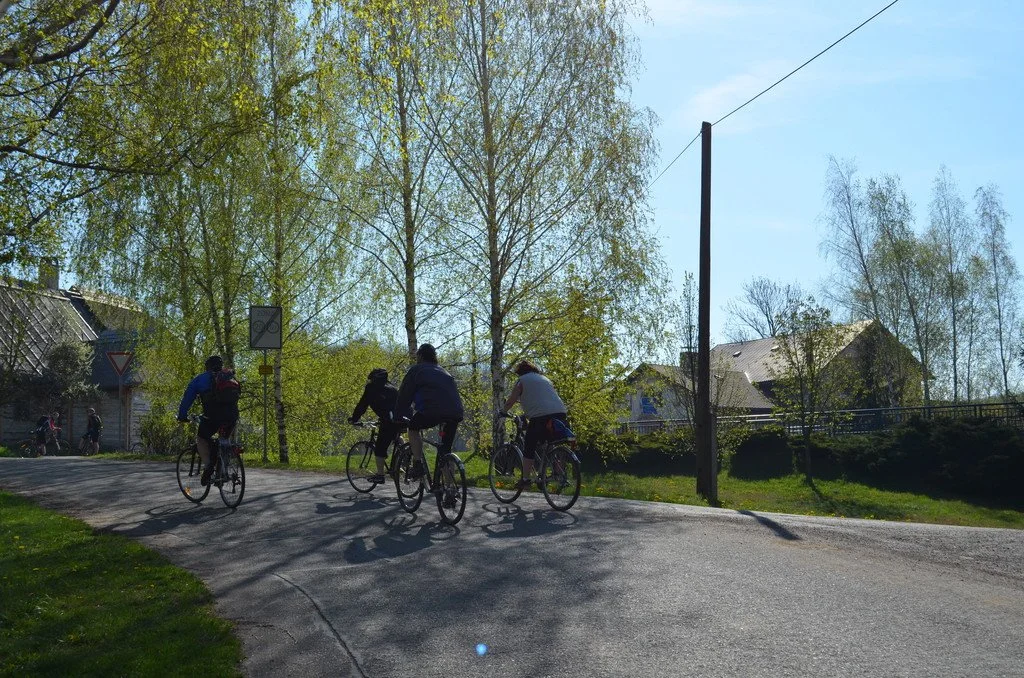 Cyklisté jedou ulicí kolem rodinných domů