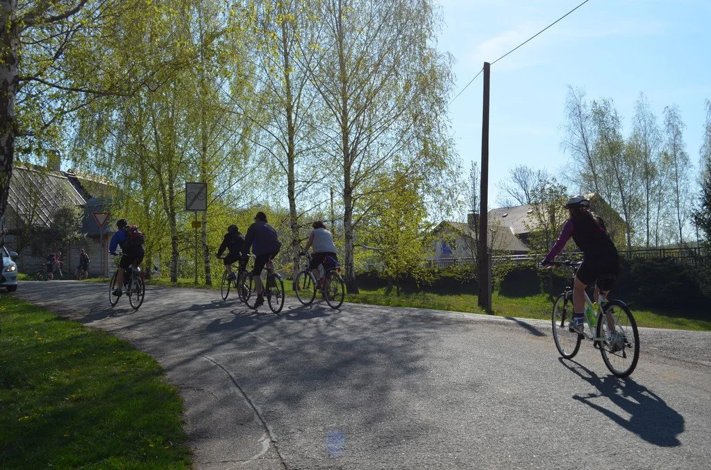 Skupina cyklistů projíždí vesnickou ulicí na jaře