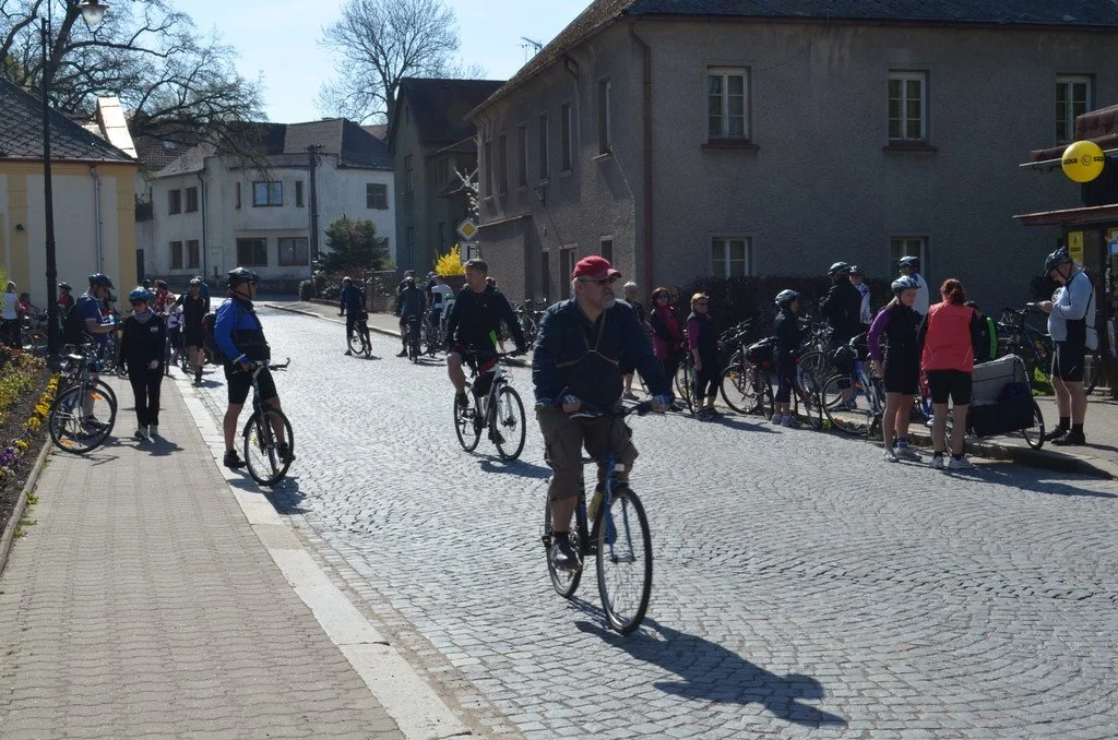 Cyklisté projíždí historickou ulicí, v pozadí zalesněný kopec