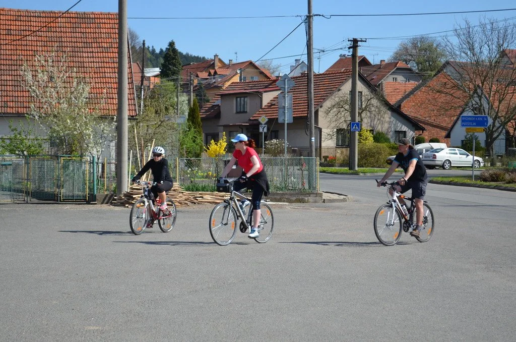 Tři cyklisté projíždějí ulicí mezi rodinnými domy