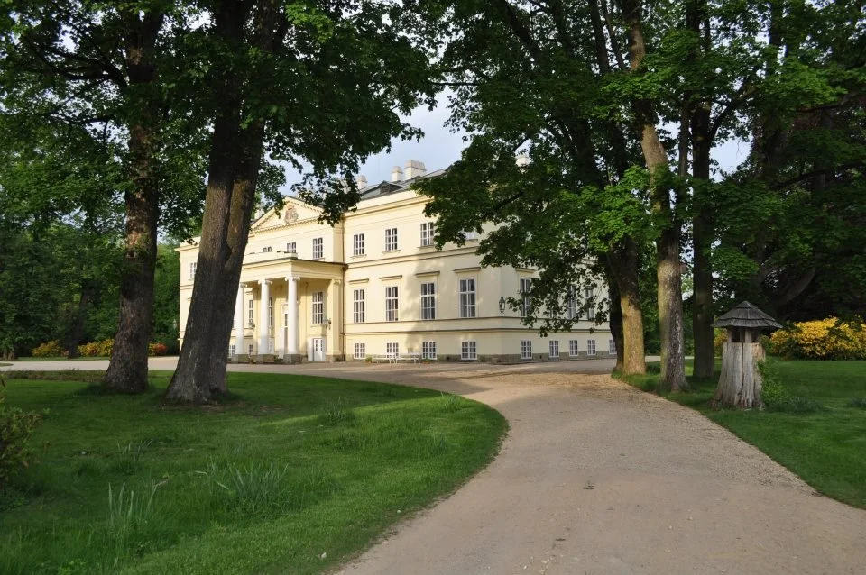 Klasicistní zámecká budova s kolonádou uprostřed vzrostlého parku