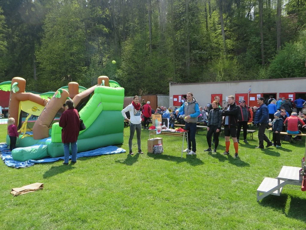 Nafukovací skluzavka a lidé na trávě v areálu s dětským odpolednem