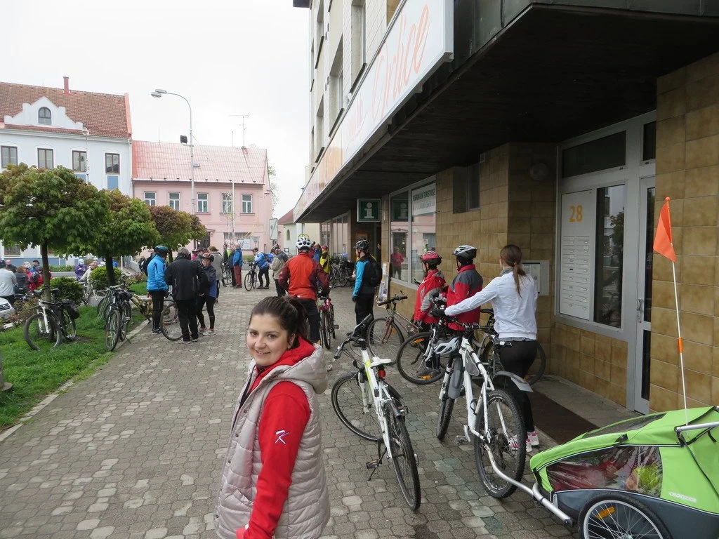 Cyklisté s koly na chodníku před domem, žena v popředí