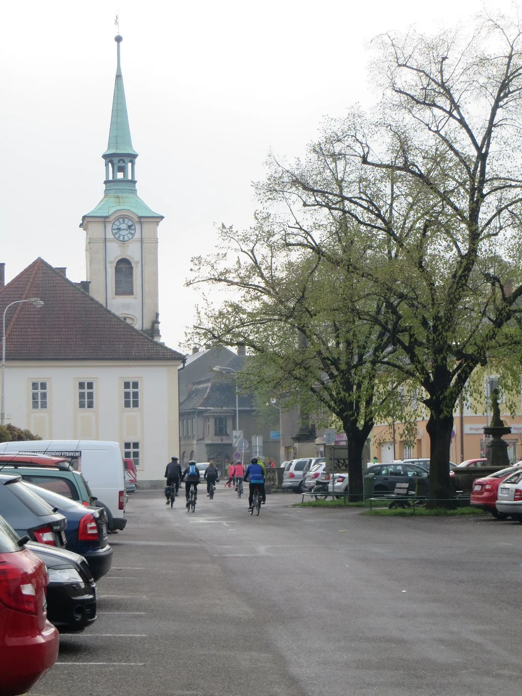Kostelní věž s hodinami a cyklisté na náměstí u parkoviště