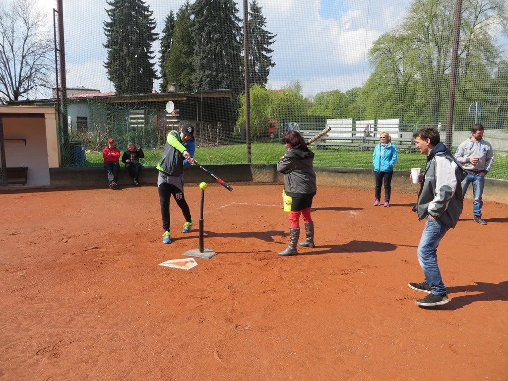 Softballový zápas, hráčka odpaluje míček ze stojanu