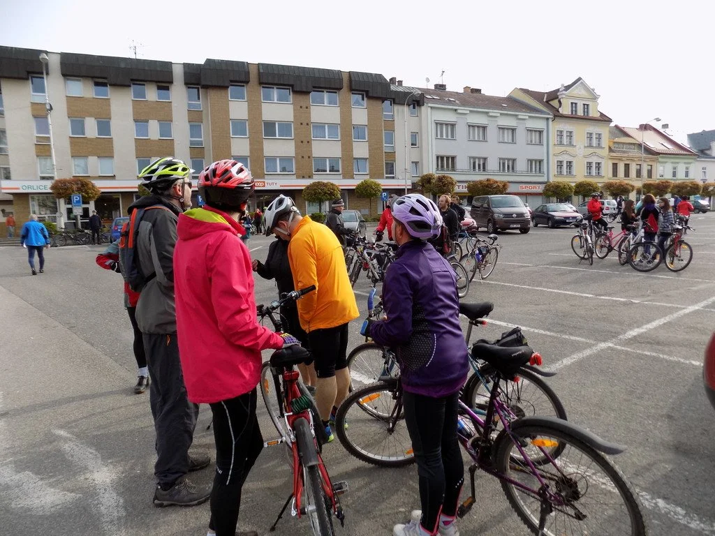 Skupina cyklistů s koly na náměstí před obchody