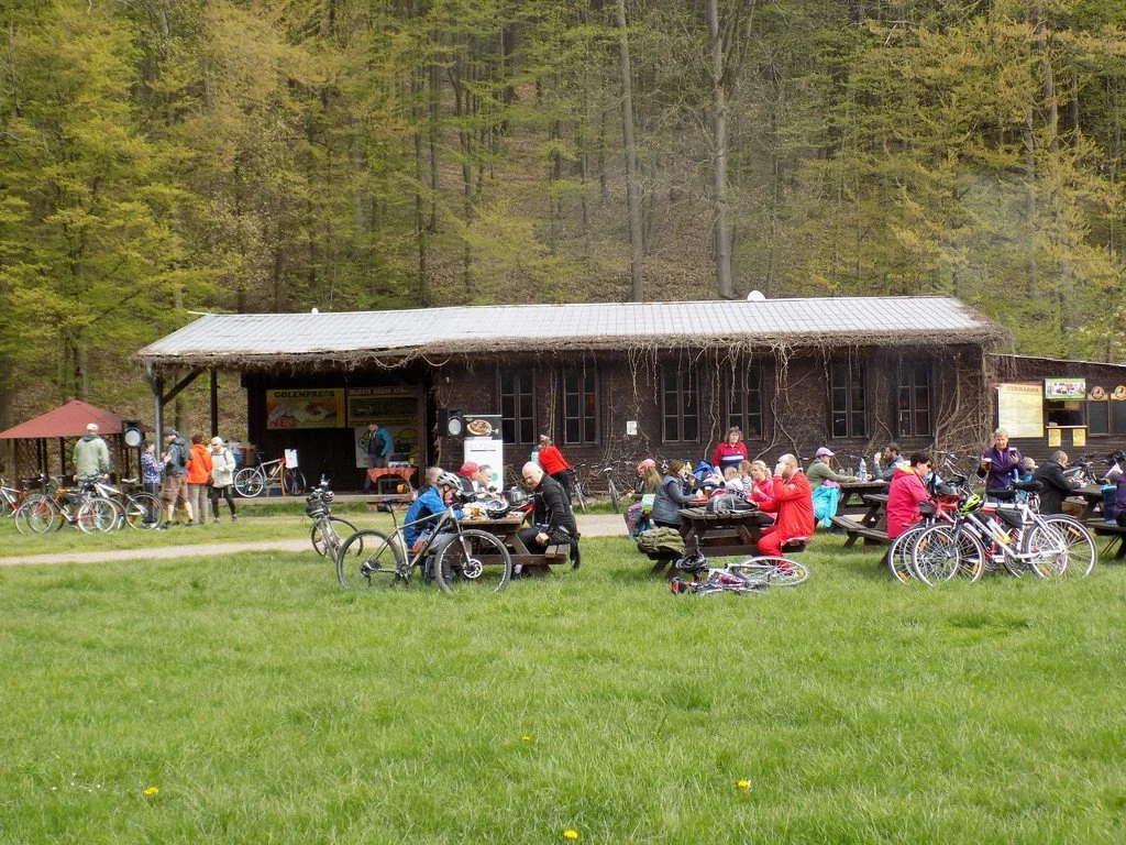 Cyklisté odpočívají u dřevěné chaty na lesní zastávce