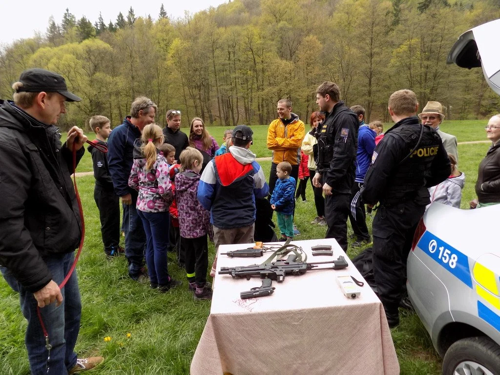 Policista prezentuje výzbroj skupině dětí a dospělých na louce