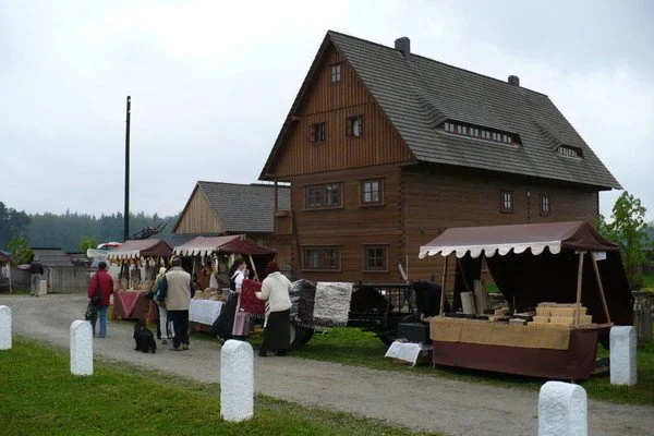 Dřevěné roubené stavení skanzenu s trhem a návštěvníky v dobových krojích