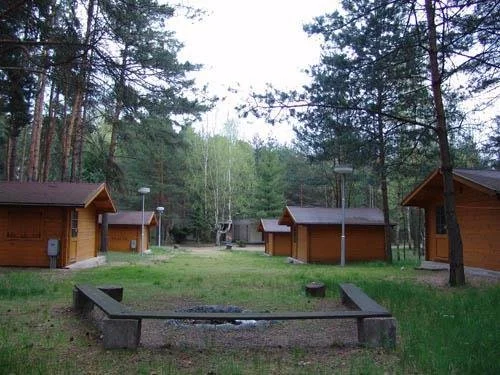 Dřevěné chatky v táborovém areálu s ohništěm a lavicemi