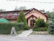 Vstup do restaurace s obloukovým portálem, živým plotem a nabídkovou tabulí