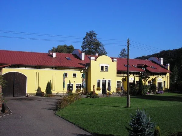 Žlutá budova s červenou střechou, terasou a upravenou zahradou