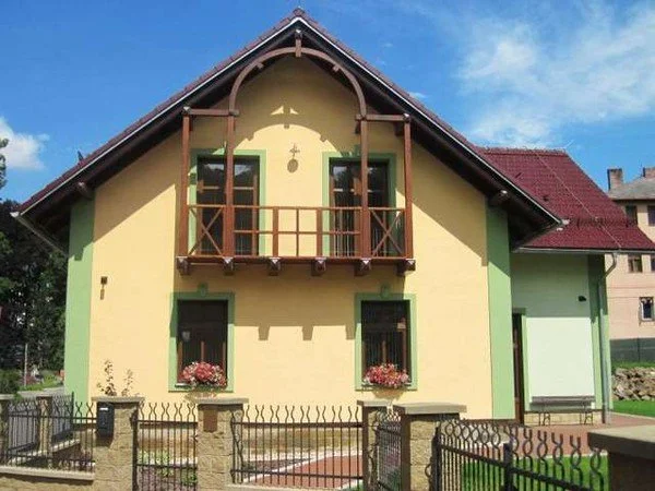 Žlutá vila se zeleným zdobeným balkonem a sedlovou střechou