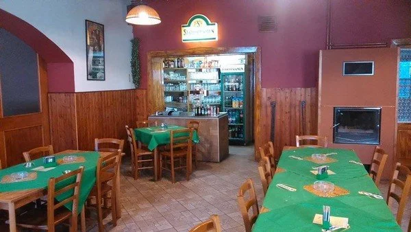 Interiér restaurace se zelenými ubrusy, dřevěným obložením a krbem