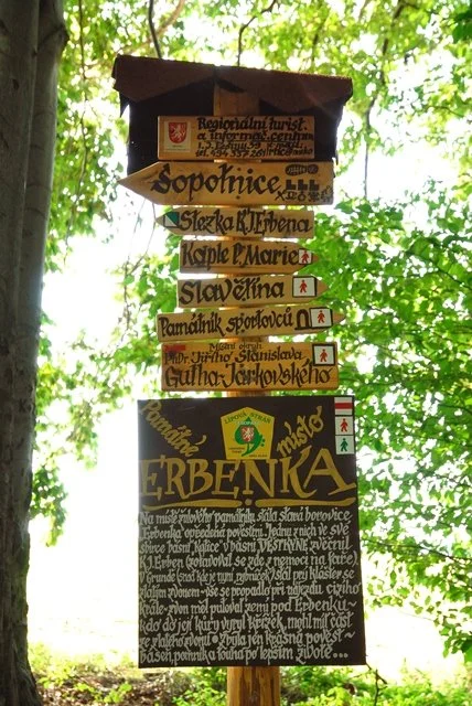 Dřevěný rozcestník s turistickými směrovkami a tabulí o Erbence