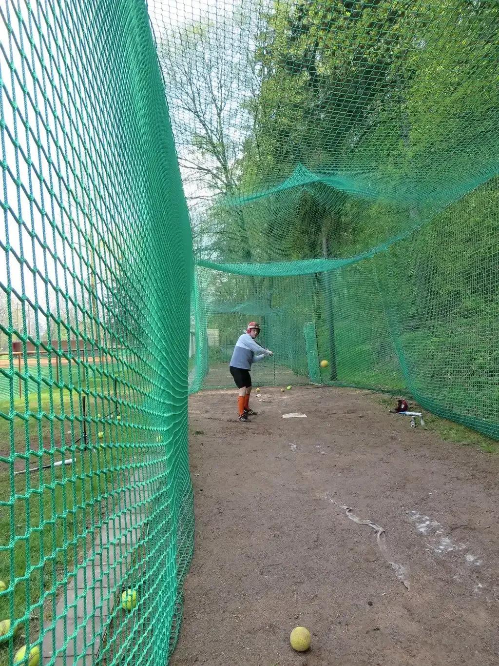 Hráč v helmě odpaluje míček v softballové tréninkové kleci