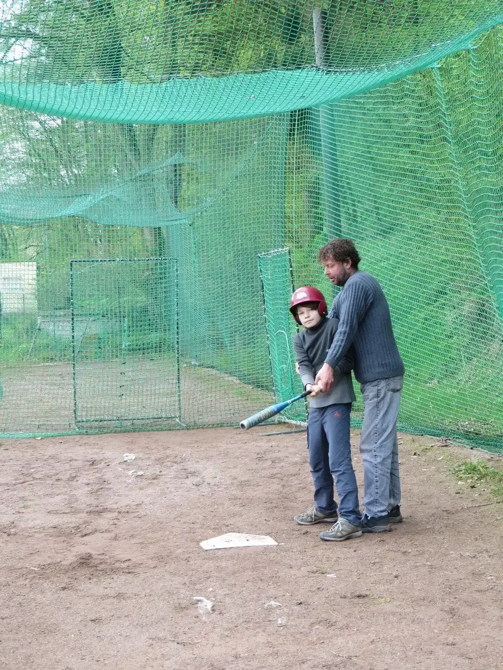 Otec pomáhá chlapci s odpalovací pálkou v softballové kleci