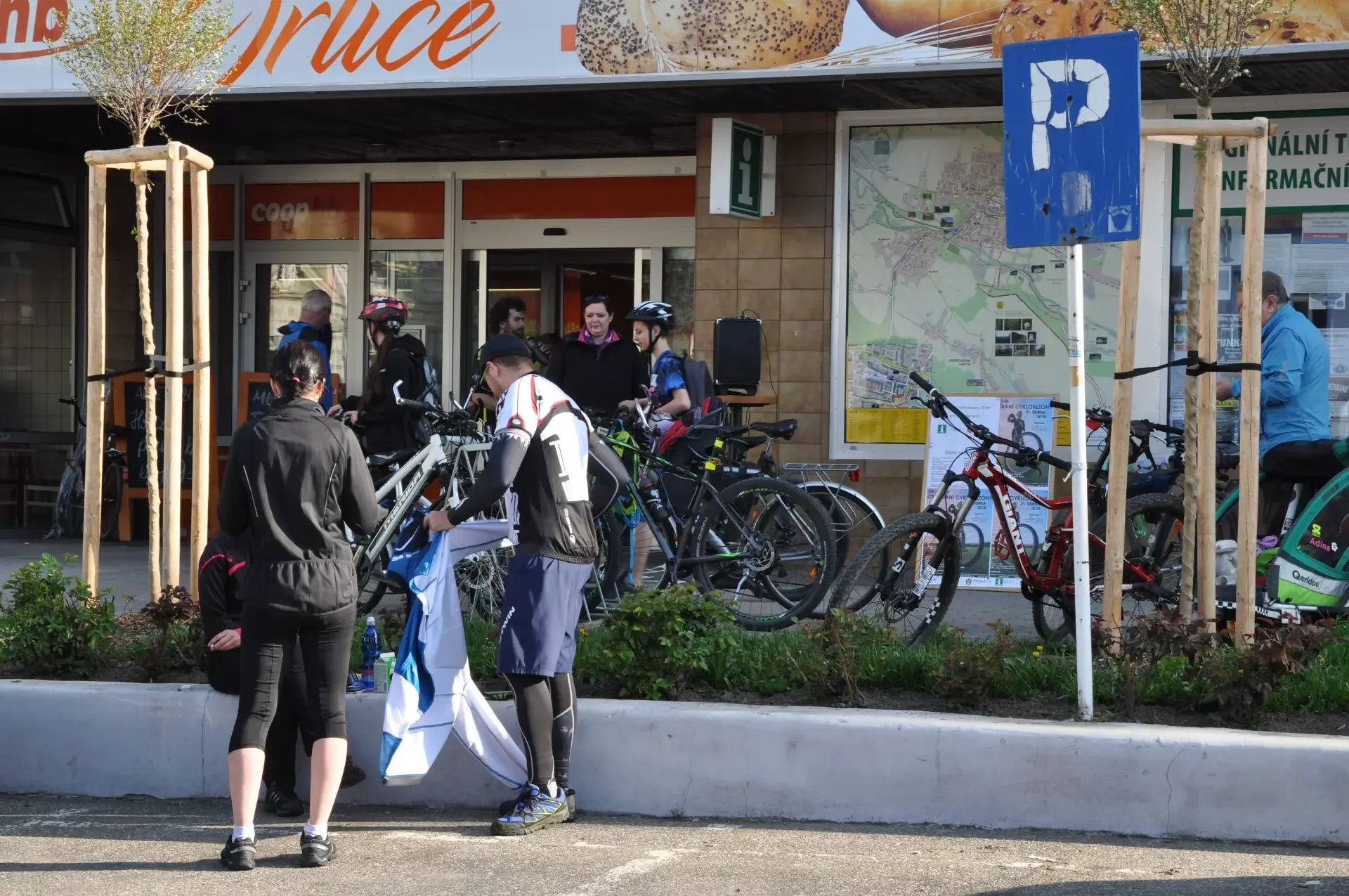 Cyklisté s koly před obchodem a informační tabulí s mapou