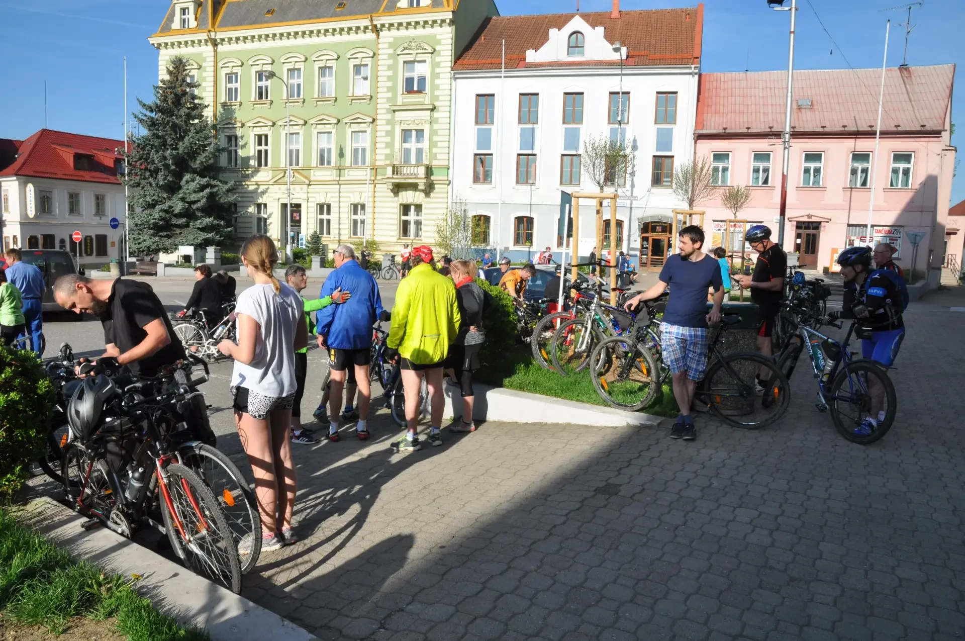 Cyklisté s koly před historickými domy na náměstí
