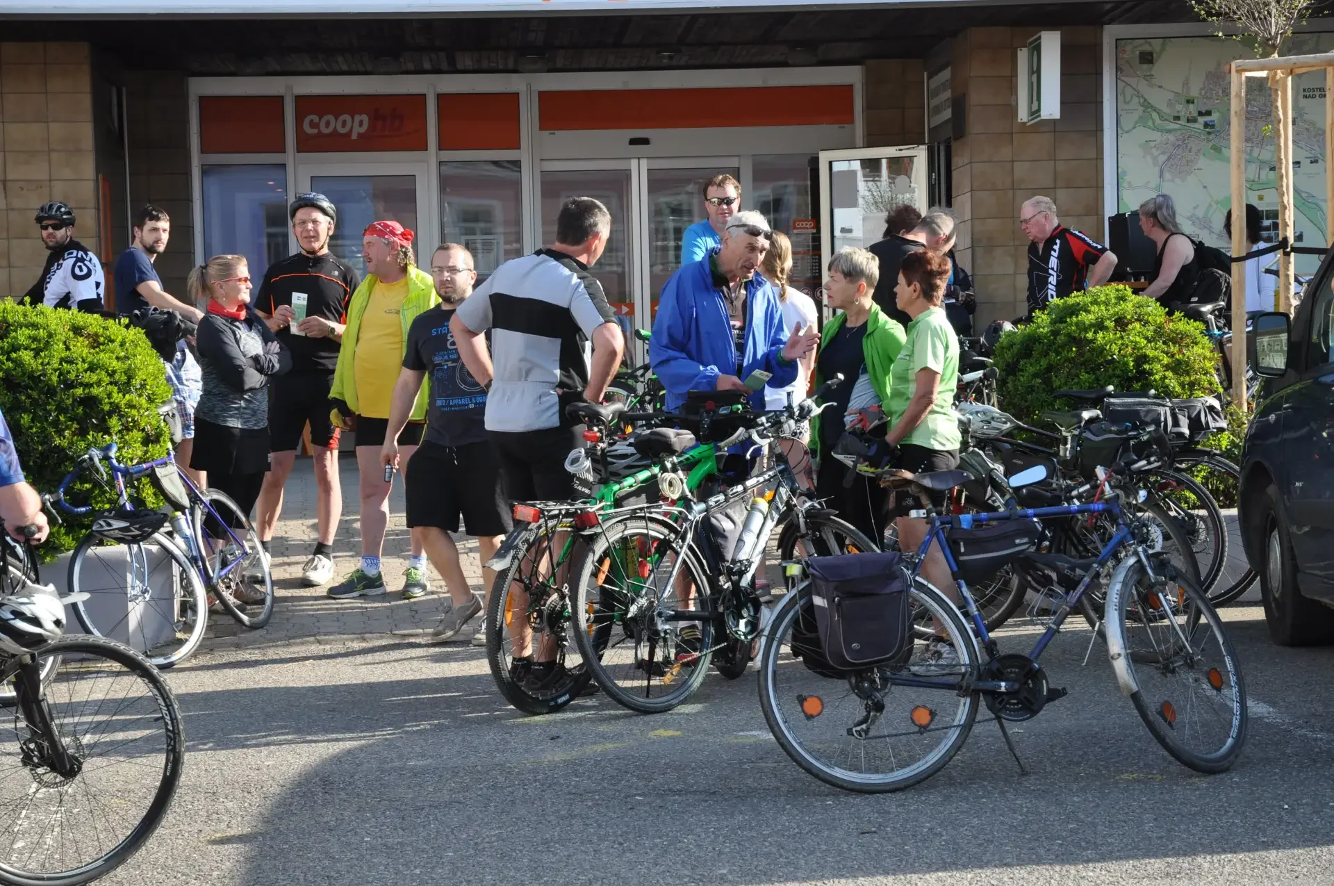 Skupina cyklistů diskutuje před prodejnou Coop při zastávce na trase