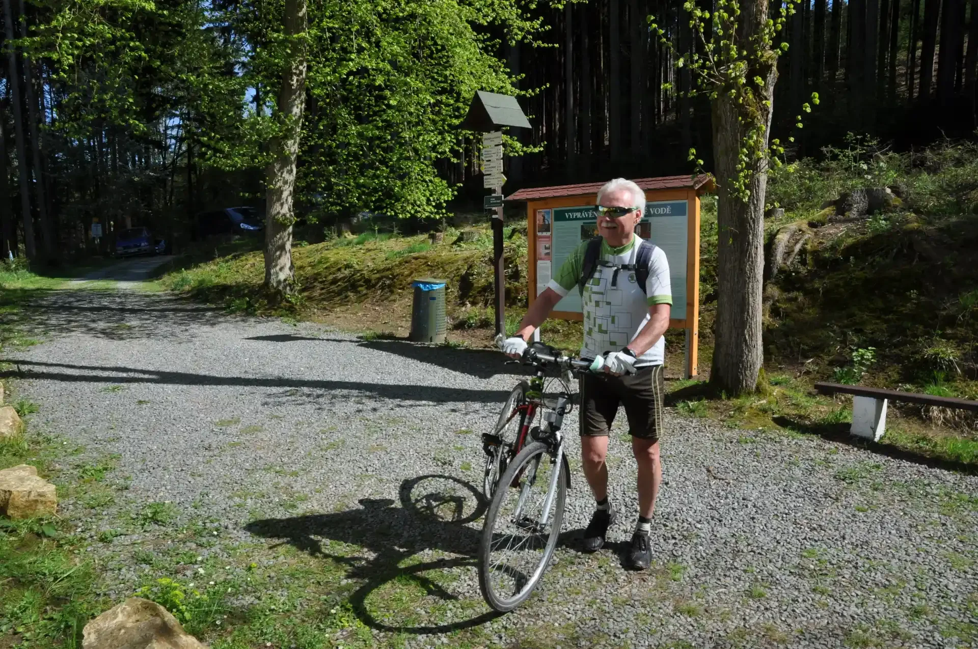 Cyklista s kolem stojí u lesní informační tabule s pověstmi o vodě
