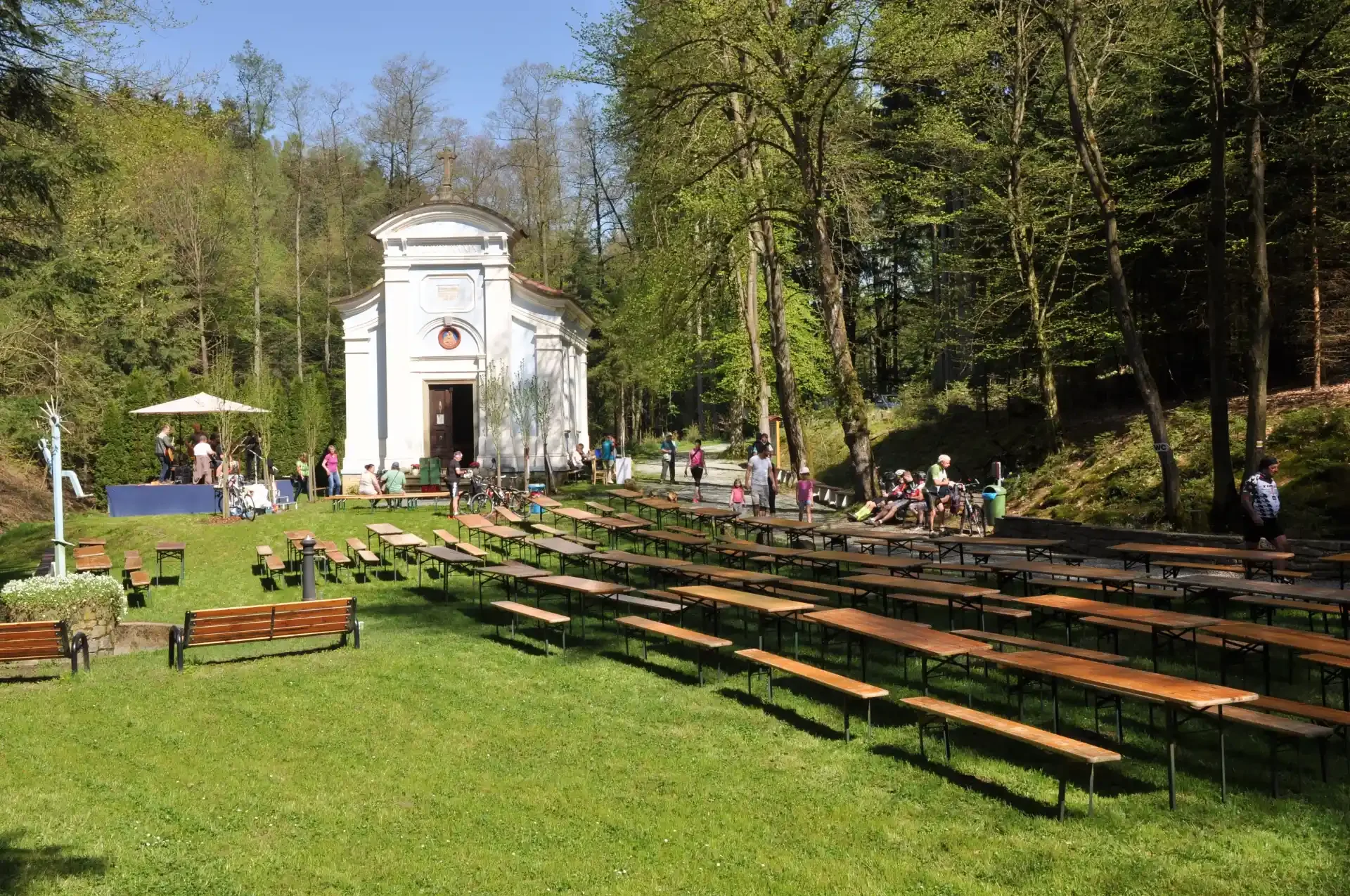 Bílá kaple v lese a řady prázdných stolů připravených na akci