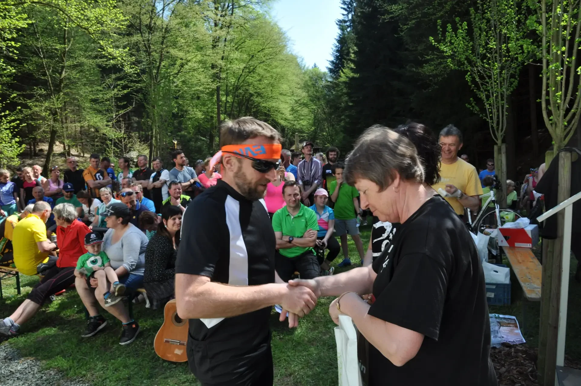 Cyklista si podává ruku s pořadatelkou při předávání ceny v lese