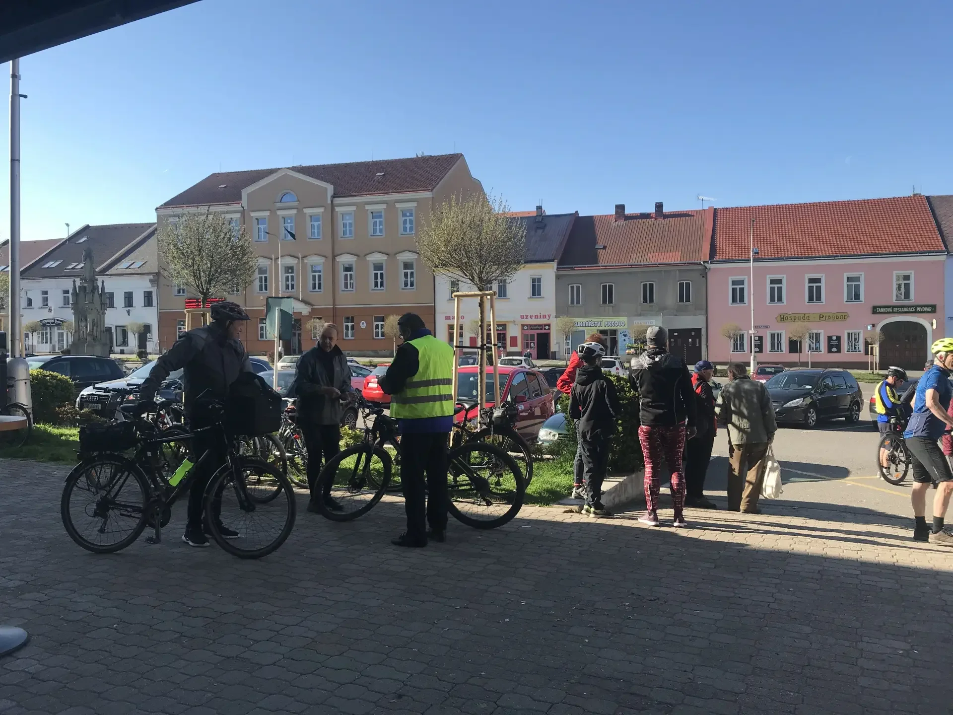 Skupina cyklistů s koly na náměstí před barevnými domy