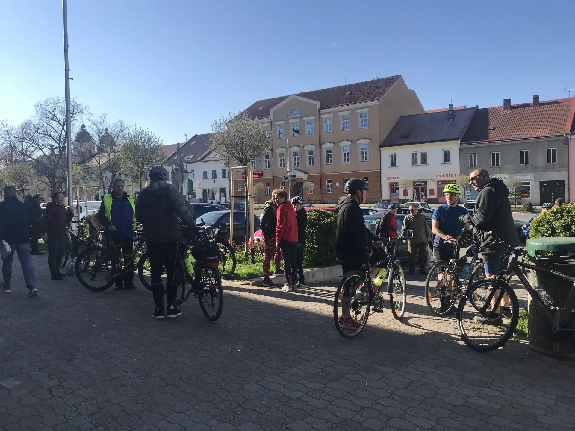 Cyklisté na náměstí, v pozadí kostelní věž a historické domy