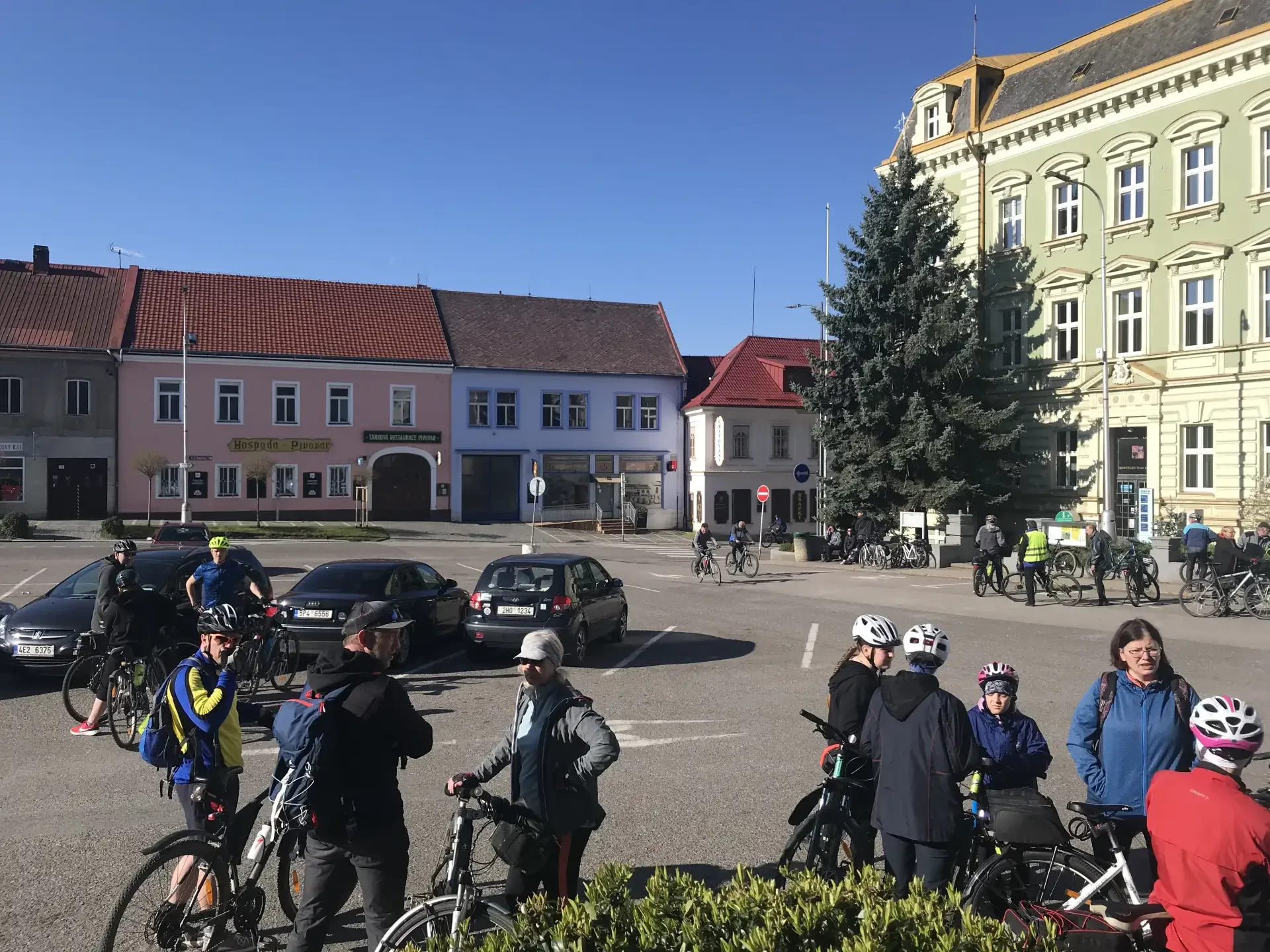 Skupina cyklistů s koly na náměstí před zelenou budovou