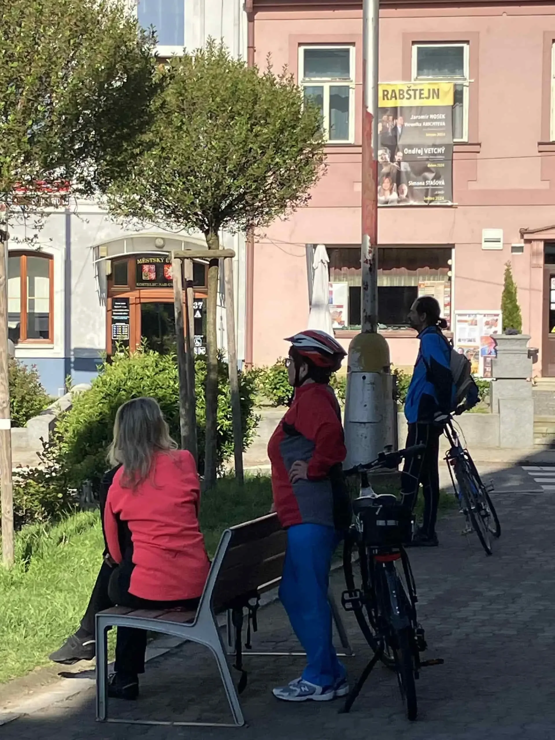 Cyklisté odpočívají na náměstí u plakátu Rabštejn