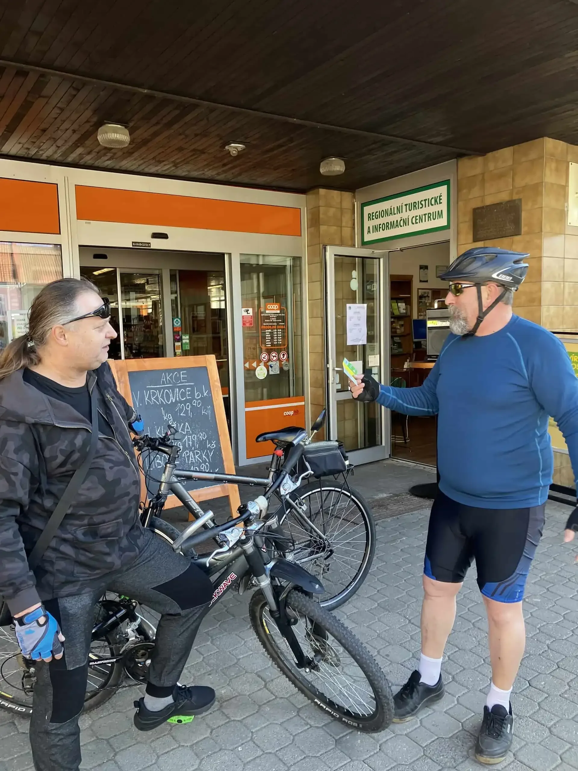 Cyklista předává jízdenku dalšímu cyklistovi před informačním centrem