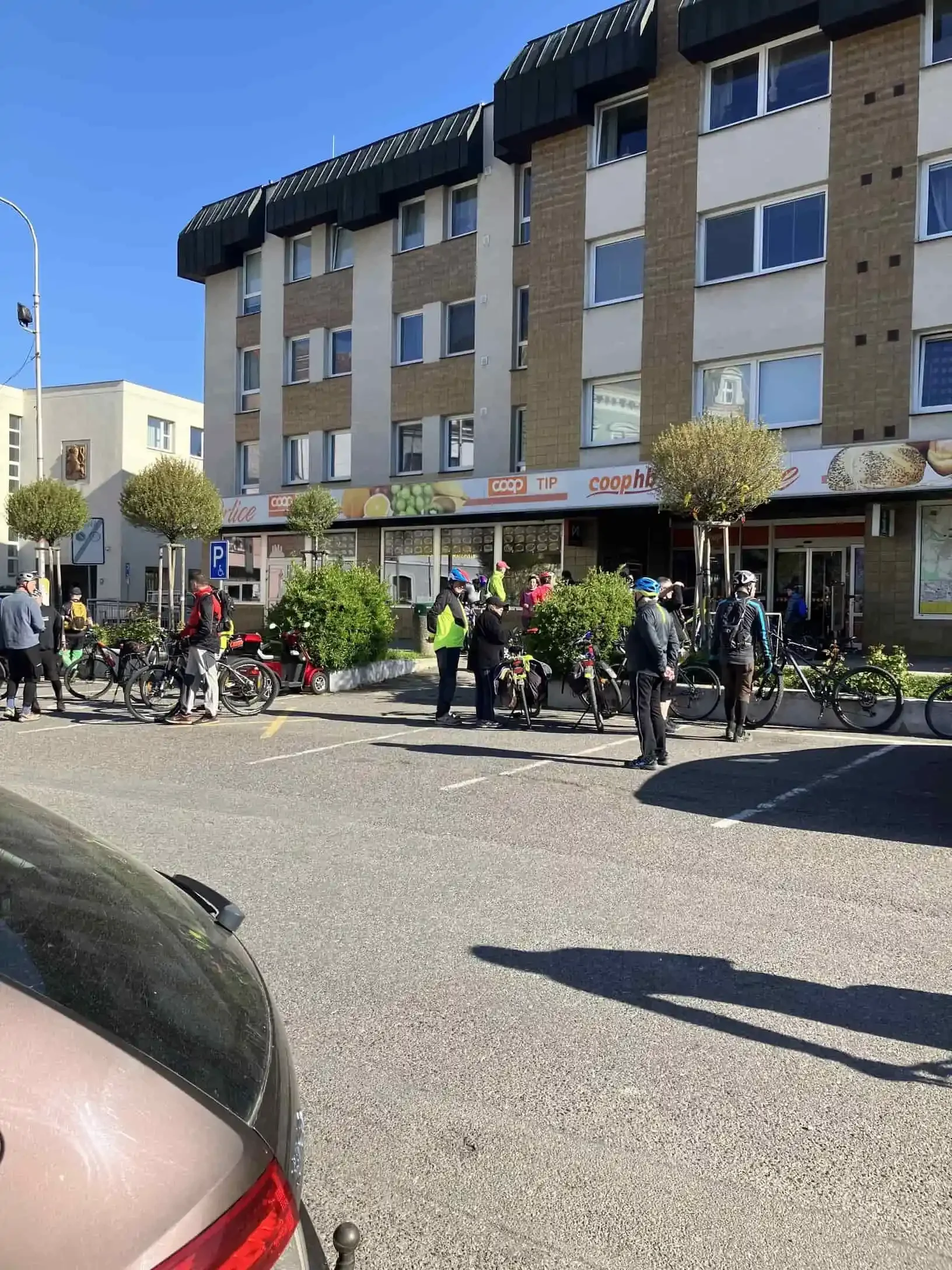 Skupina cyklistů před vchodem do obchodu COOP