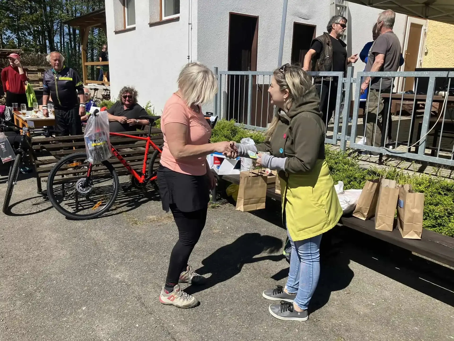 Žena v žlutozelené zástěře předává výherní tašku cyklistce