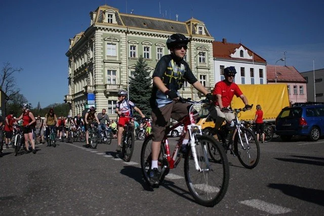Cyklisté na kolech před historickou žlutozelenou budovou na náměstí