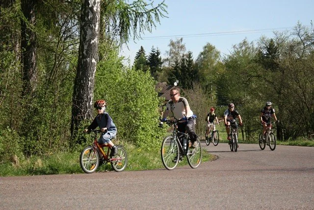 Chlapec a dospělí cyklisté jedou po silnici kolem lesa