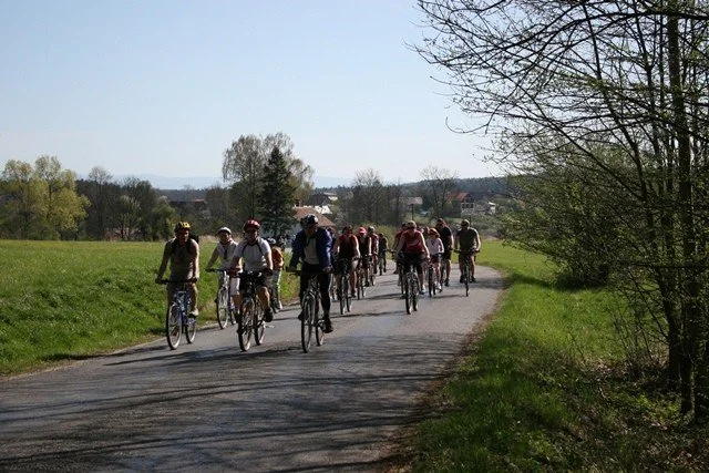 Zástup cyklistů jede po polní cestě mezi loukami