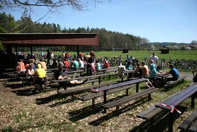 Lidé sedí na lavičkách u sportovního hřiště s odstavenými koly